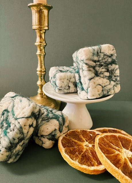Marble-patterned woolen soap bars on a white stand with dried oranges on a green surface.