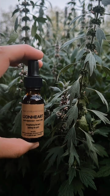 Hand holding a bottle labeled 'Lionheart' in front of green plants