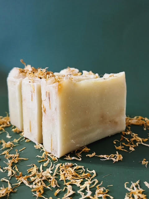 Three bars of soap with dried flowers on a dark green background
